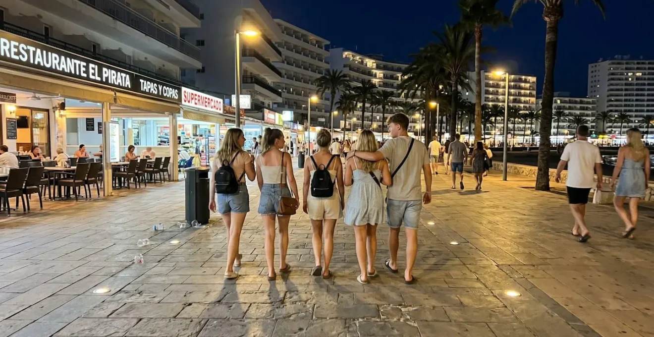 Gruppe junger Urlauber läuft nachts auf beleuchteter Promenade in Magaluf zwischen Hotels und Ausgehviertel