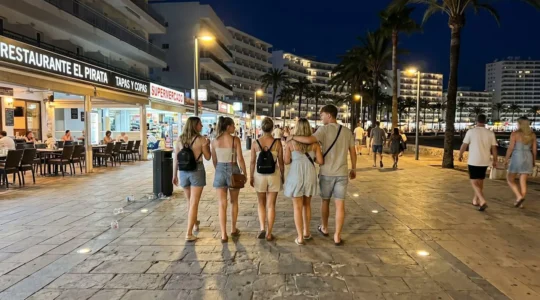 Gruppe junger Urlauber läuft nachts auf beleuchteter Promenade in Magaluf zwischen Hotels und Ausgehviertel